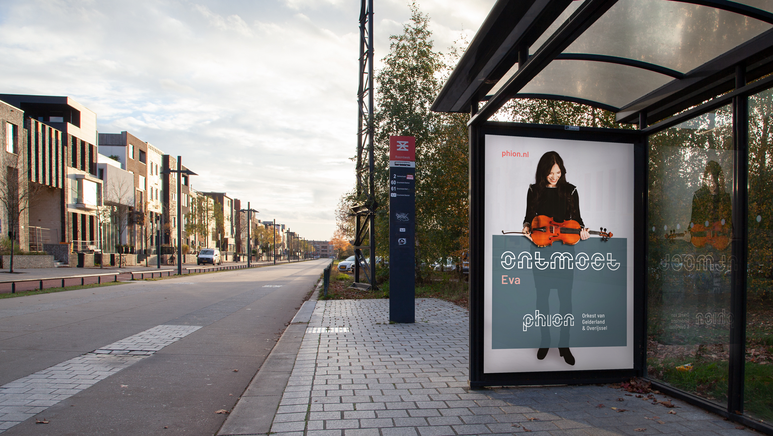 Bushokje met reclamebord waar een vrouw uit het orkest met haar viool opstaat