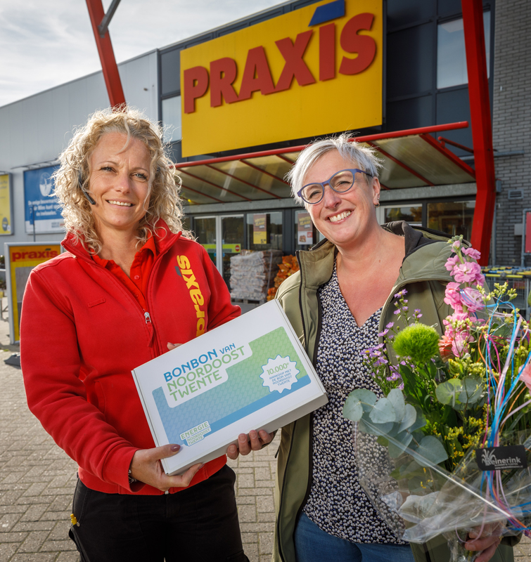 Medewerker van de Praxis die de bon van Noordoost Twente vasthoudt en een vrouw die een bos bloemen vasthoudt staan voor de Praxis