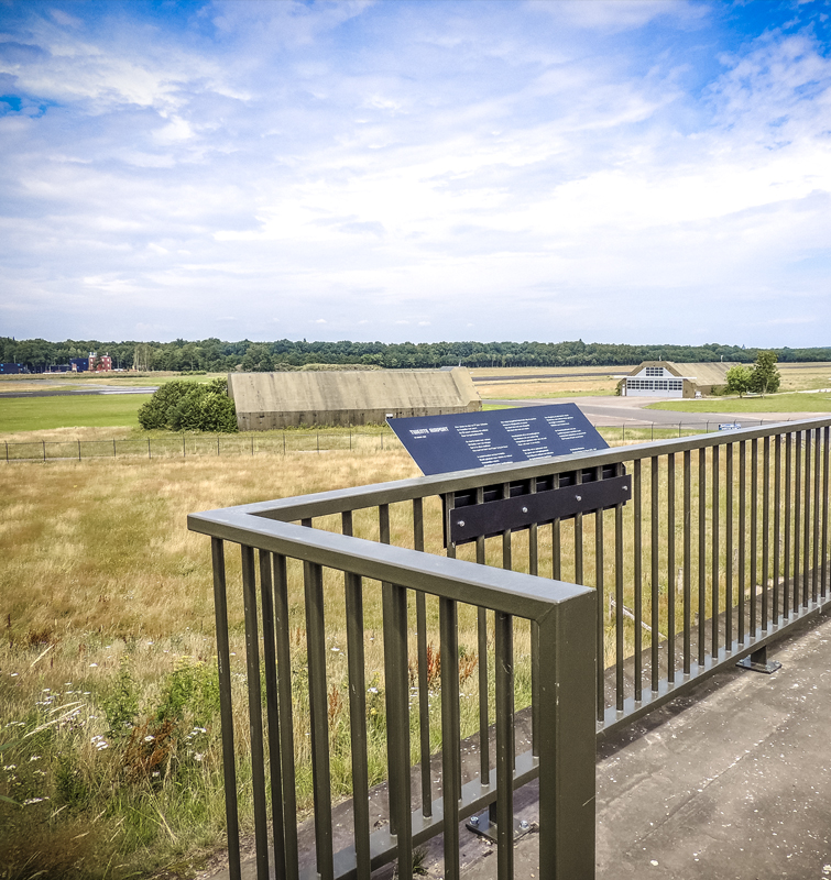 Hek bovenop een hangar met een informatief bord met in de verte twee andere hangars