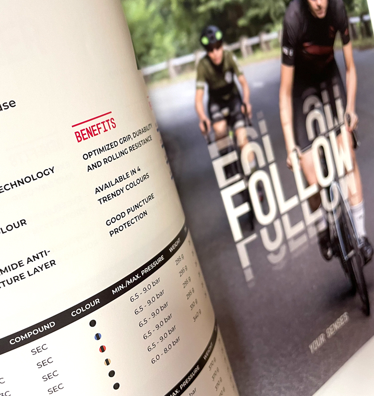 Opengeslagen catalogus ingezoomd op een afbeelding van twee mensen op een mountainbike op de weg